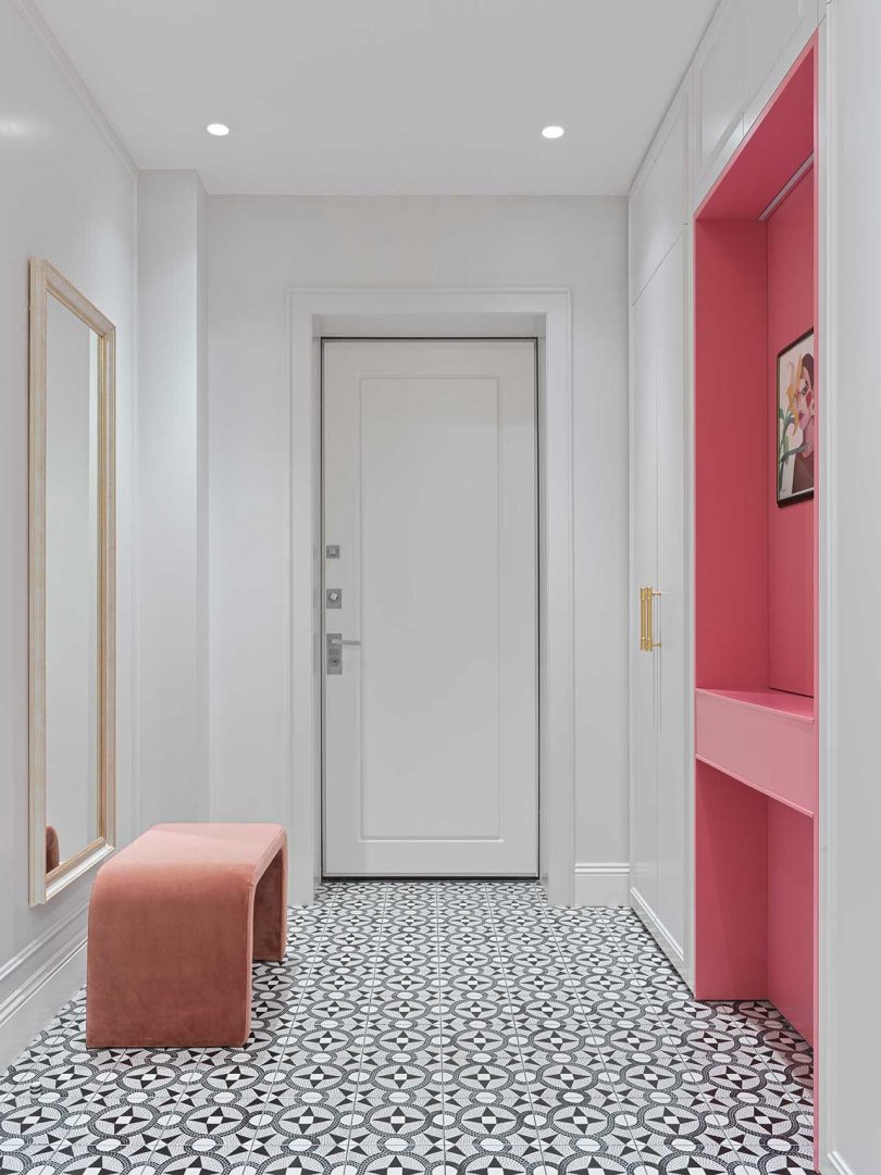The entryway shows off a pink vanity, a pink bench, a mirror and hidden storage and black and white tiles