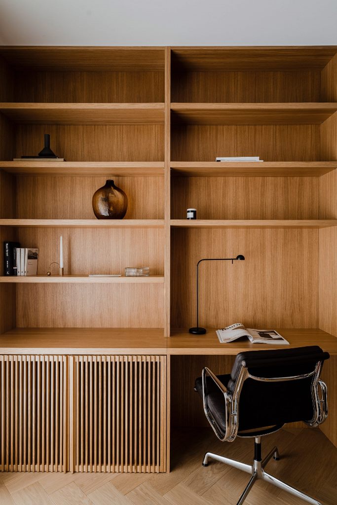 The home office is done with wood, there are open and closed storage units and a stunning black chair