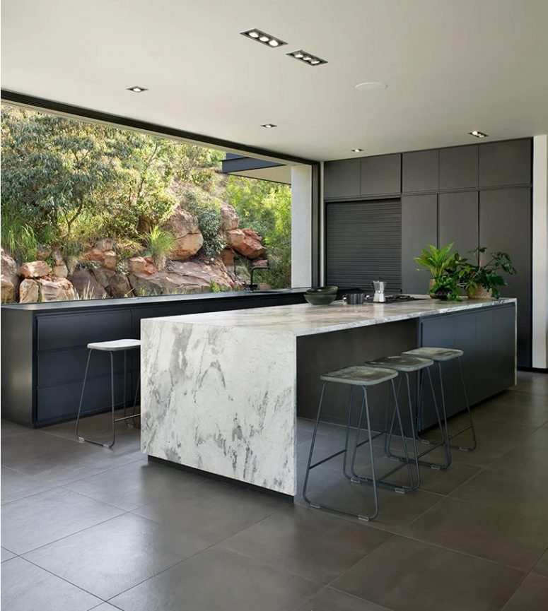 The kitchen is done with graphite grey cabinets, a large kitchen island with a white marble countertop