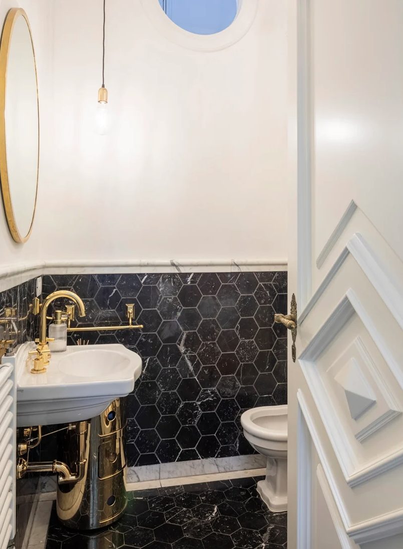 The bathroom is clad with black marble tiles, there are some gold touches that echo with apartment