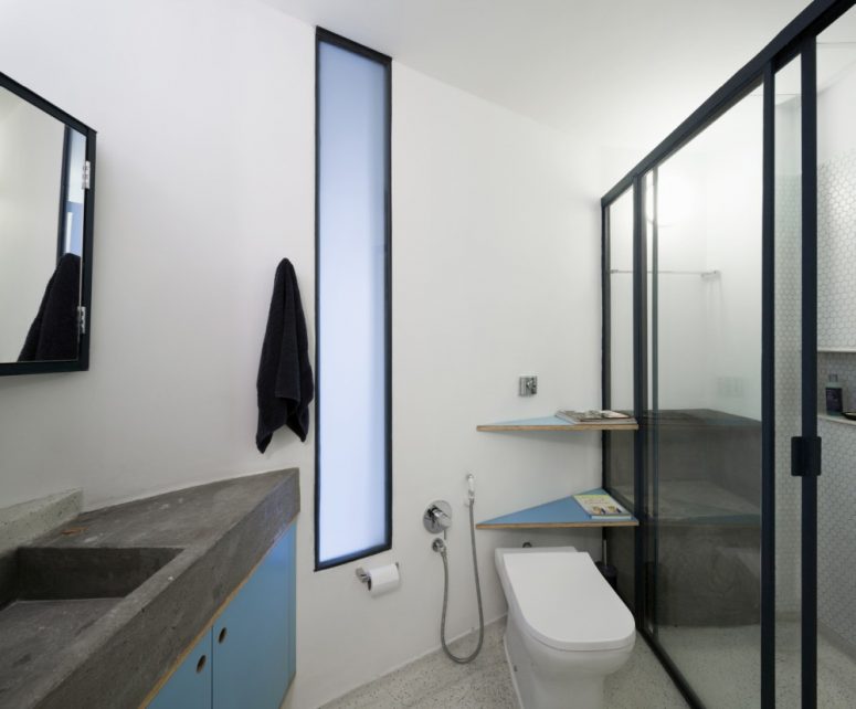 The bathroom is small, done in grey, white and blue with concrete countertops and a comfy shower