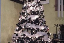 a black Christmas tree with black and white ornaments, white cotton snow, a swirled top and striped ribbons