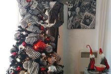 a black Christmas tree with striped ribbons, gold, silver, red and black ornaments and a Jack Skellington figure next to it