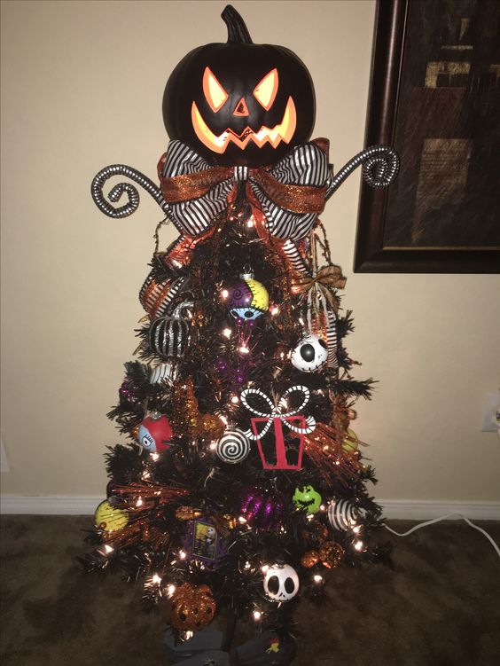 a black Halloween or Christmas tree decorated with Nightmare Before Christmas ornaments, lights, a bow and a giant pumpkin