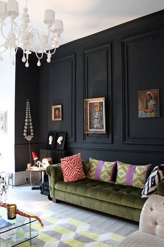 a black panel wall makes a statement in this space, with neutrals and muted colors, a green sofa and refined artworks