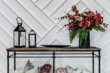 a chic entryway with a white paneled wall, an industrial console table, baskets with pillows and a bold floral arrangement