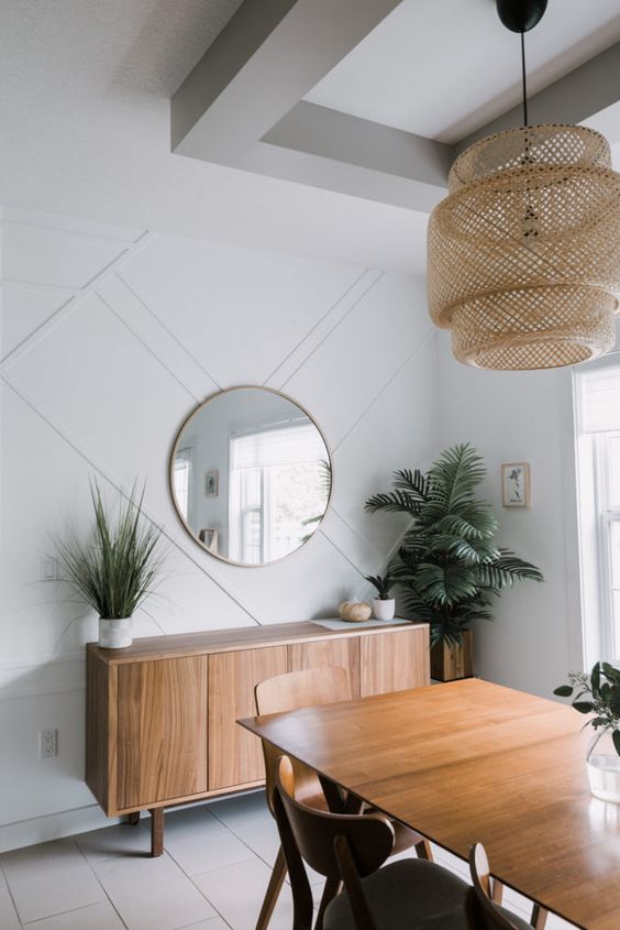 A chic mid century modern dining room with a white paneled wall, elegant wooden furniture, a wicker pendant lamp and greenery