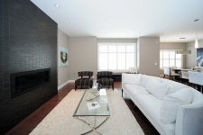 a contemporary living room with a black tile fireplace wall, a large curved sofa in white and elegant furniture around