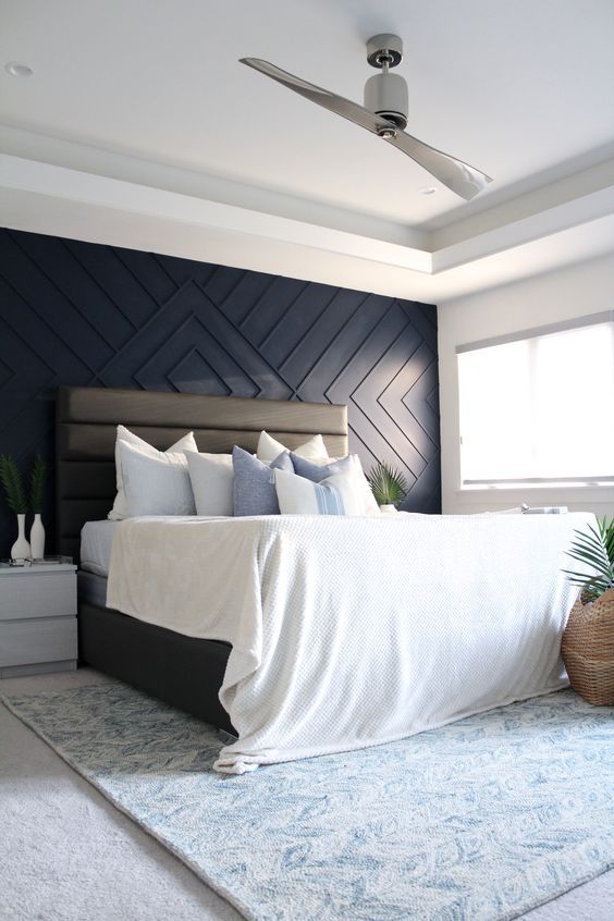 a cozy and airy bedroom with a navy geometric paneled wall, a leather upholstered bed, neutral nightstands, greenery in vases and pots