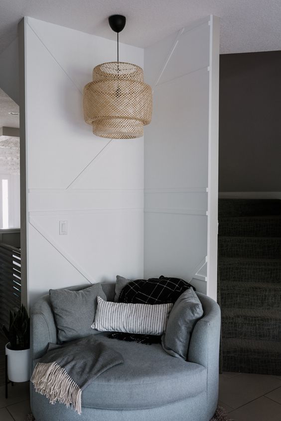 a cozy reading nook with a white geometric wall, a pendant wicker lamp and a grey round chair is very welcoming