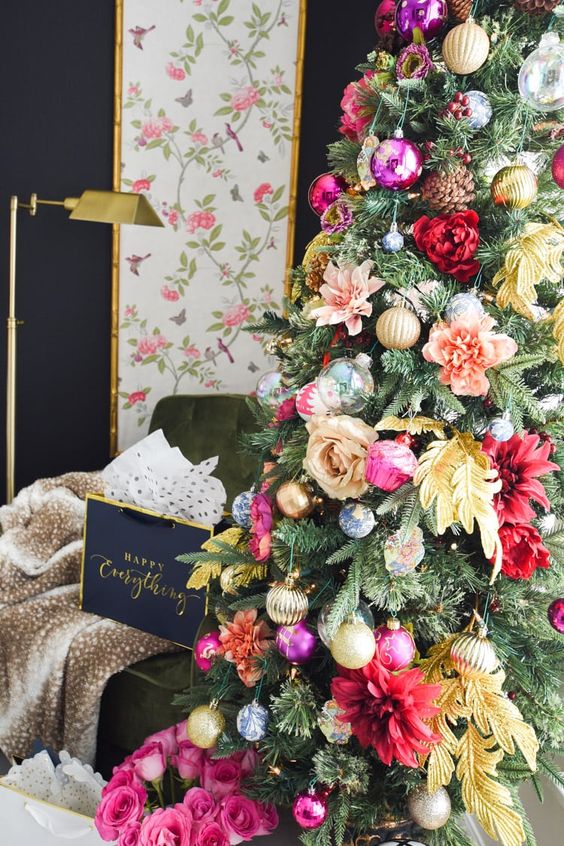 a glam Christmas tree decorated with pink, red, peachy and yellow blooms, leaves, shiny metallic and bold ornament and pinecones