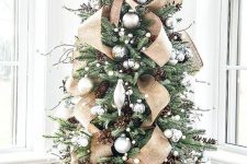 a gorgeous tabletop Christmas tree with silver ornaments, burlap ribbons, snowball garlands, pinecones and a large burlap bow on top