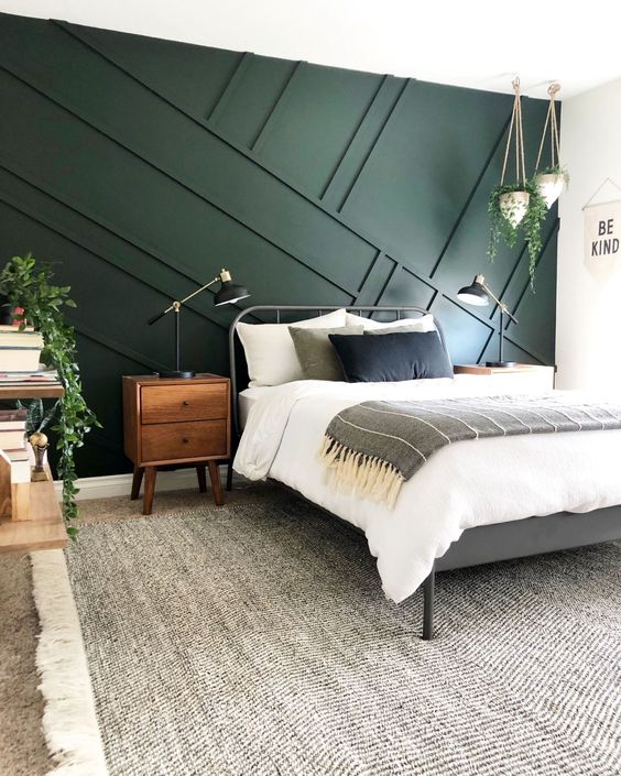 A mid centiry modern bedroom with a dark green geometric panel wall, a metal bed, wooden furniture and some greenery in pots to enliven it