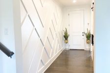 a mid-centiry modern entryway with a white paneled geometric wall and statement plants in gold pots is very elegant
