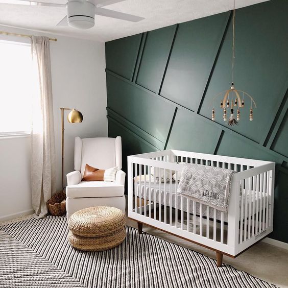 a mid-century modern nursery with a green paneled wall, neutral furniture, wicker ottomans, a wooden mobile and a brass floor lamp
