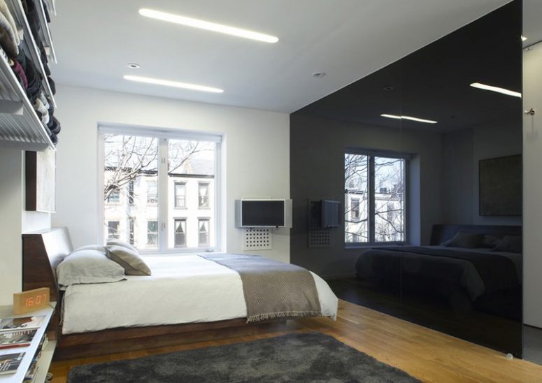 a minimalist monochromatic bedroom with a glossy black wall that brings drama and may hide a bathroom