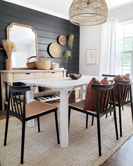 a modern farmhouse dining space with a black plank wall and black chairs that echo with it and add drama to the space