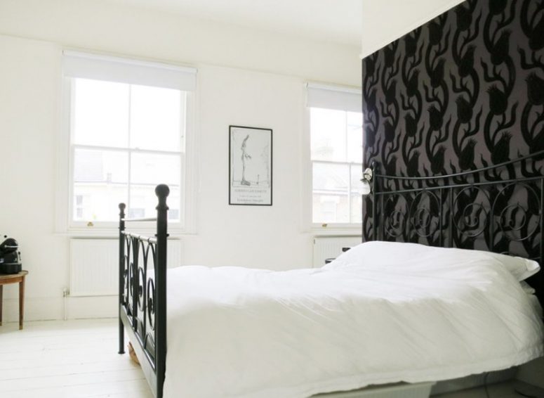 a monochromatic vintage-inspired bedroom with a black floral wallpaper wall, a black forged bed and a chic artwork