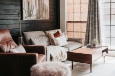 a neutral and warm-colored living room with a black plank wall, neutral furniture, pink and terracotta textiles and upholstery