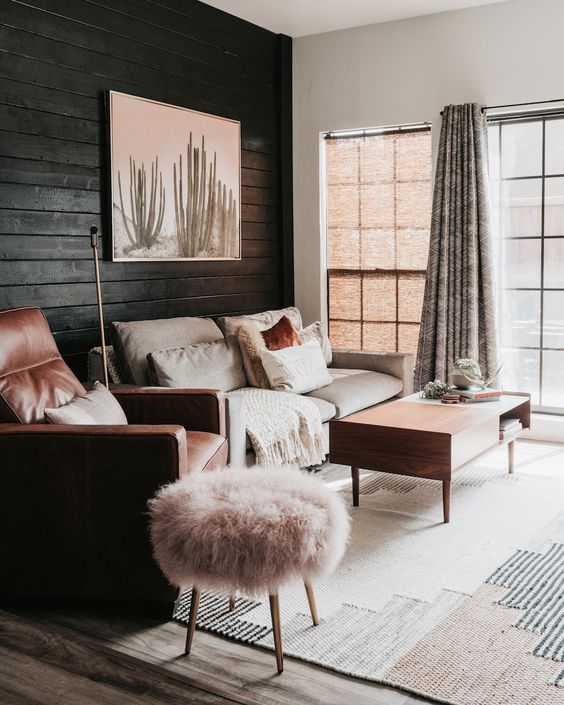 A neutral and warm colored living room with a black plank wall, neutral furniture, pink and terracotta textiles and upholstery