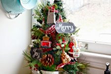 a pretty tabletop Christmas tree decorated with pinecones and mini kitchen appliances, berries in a bucket is a lovely vintage idea