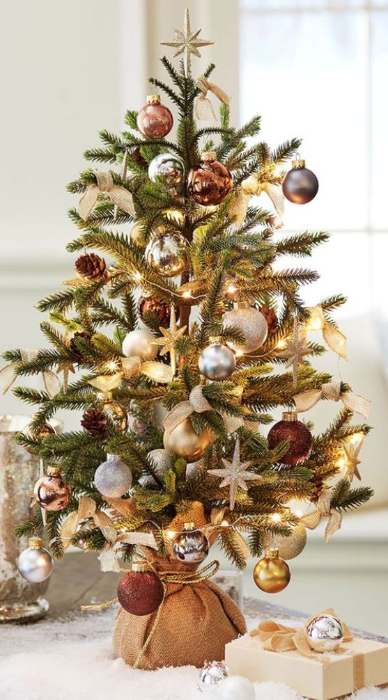 a pretty tabletop Christmas tree with lights, gold and silver ornaments, pinecones and copper touches wrapped in burlap