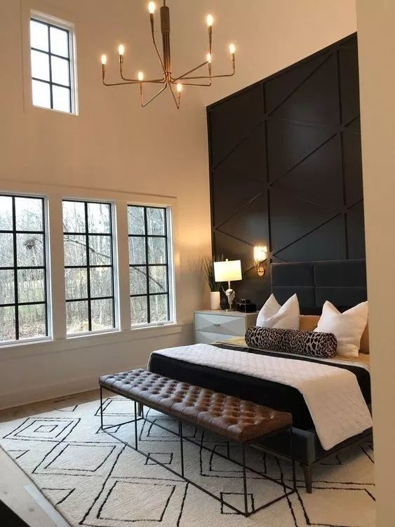 a refined bedroom with a black paneled geometric wall, a black upholstered bed, a leather bench and a catchy chandelier