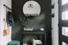 a small modern entryway with a dark green geometric wall, a black console, a green ottoman and potted greenery