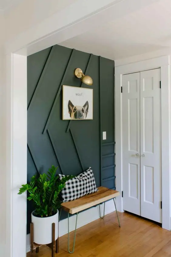 a stylish contemporary entryway with a black paneled wall, a small bench, a sconce and potted greenery is very cool