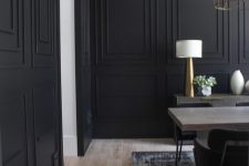 a stylish formal dining room with black paneled walls, a wooden table, a credenza and some gilded lamps