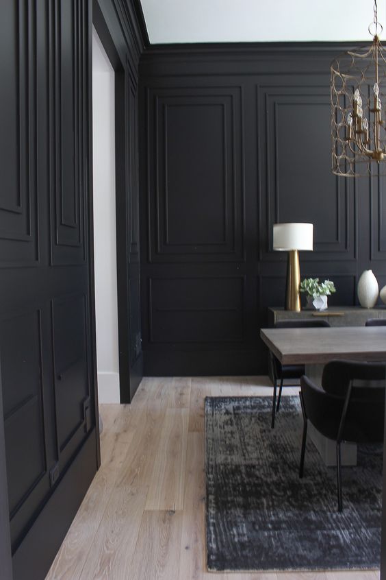 a stylish formal dining room with black paneled walls, a wooden table, a credenza and some gilded lamps
