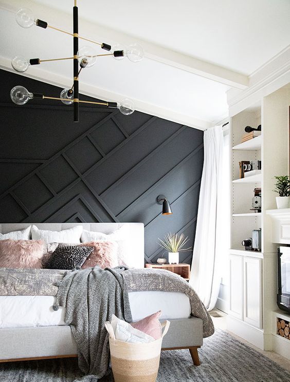 a stylish mid-century modern bedroom with a black paneled wall, an upholstered bed, built-in shelves and a stylish chandelier