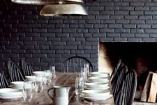 a vintage meets rustic dining room with a black brick wall, a wooden table and dark vintage chairs is very cozy