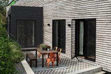 02 The exterior of the house is contrasting, dark and light, with a terrace with a wooden table and orange chairs