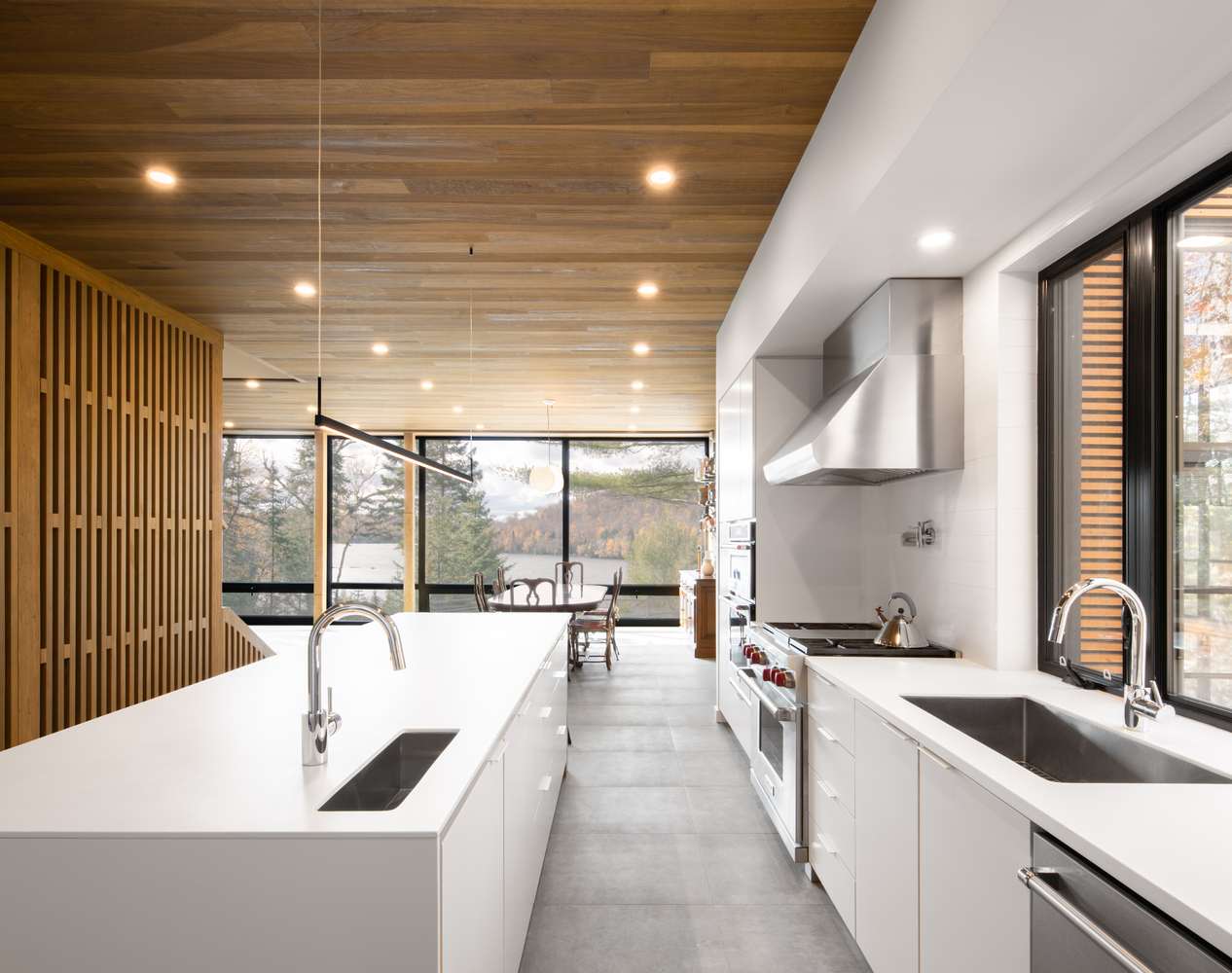 The kitchen is done with sleek white cabinets, a wooden ceiling and a concrete floor plus a wooden space divider