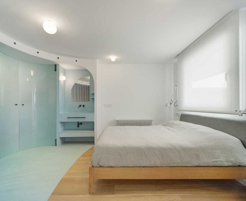 The bedroom shows off a wooden bed and sconces and the part of the room is taken curved blue doors to the bathroom