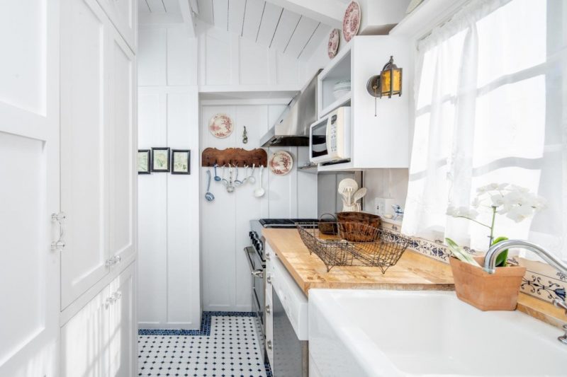 The kitchen is white, with a wooden countertop, a printed tile floor and it's small yet cozy