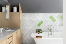 07 The bathroom is eye-catchy, with grey walls, boldly clad tiles, penny tiles on the floor, sleek plywood cabinetry and a vintage tub