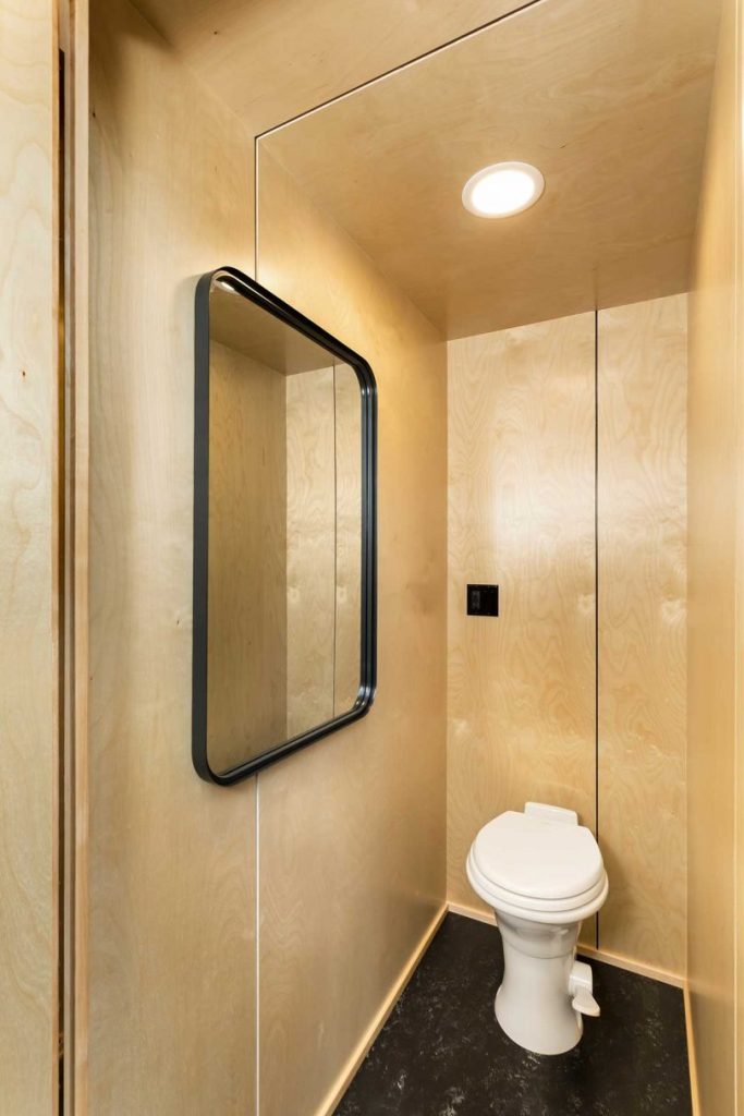 The toilet is small, with a large mirror and everything here is clad with the same plywood