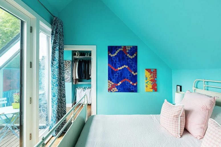This cozy bedroom is done with bright turquoise walls and a ceiling, a metal bed and bold art, there's an access to a small clsoet