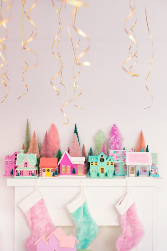a bright and fun Christmas mantel with pink and green stockings, pink and green houses and small tinsel trees for a fun touch