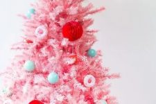 a pastel pink Christmas tree decorated with bold green, red, pastel blue ornaments and little donut ones is super cute