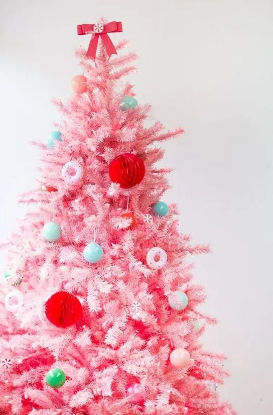 a pastel pink Christmas tree decorated with bold green, red, pastel blue ornaments and little donut ones is super cute