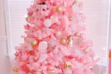 a pink Christmas tree with white and gold ornaments and some whimsical decorations plus a gold bow on top