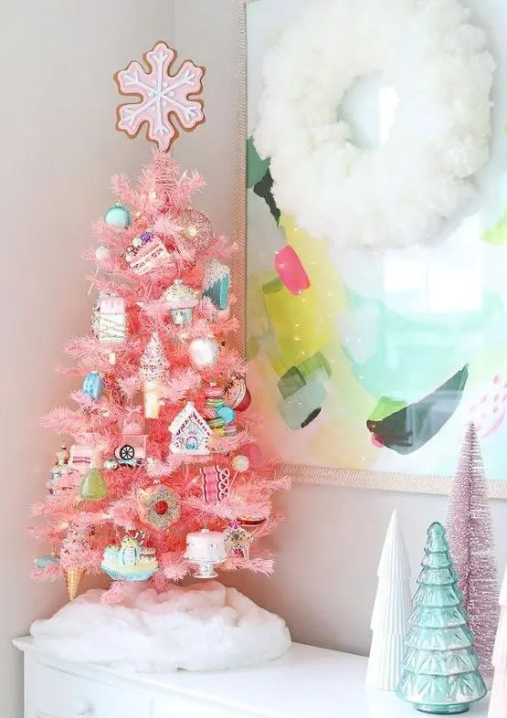 A tabletop pink Christmas tree with lights, pastel and silver food themed ornaments and a pink snowflake on top