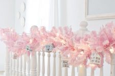 beautiful holiday railing decor with a pink fir branch garland, lights and mini houses hanging on it is a lovely idea