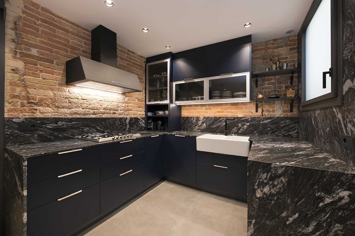 The kitchen is all industrial, with black cabinetry, black marble countertops and backsplashes, red brick walls