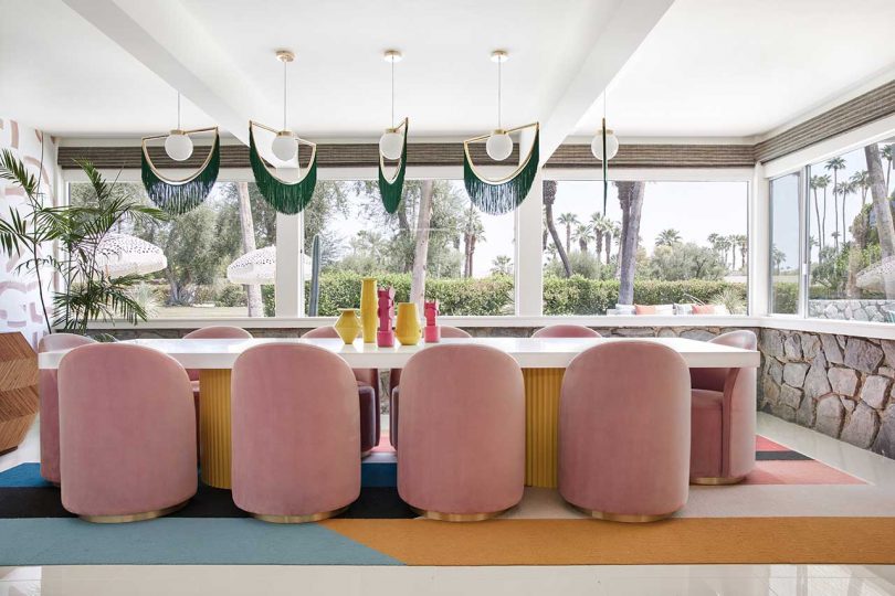 The dining space features amazing views and much light, stone in wall decor, pink chairs and pendant lamps with fringe