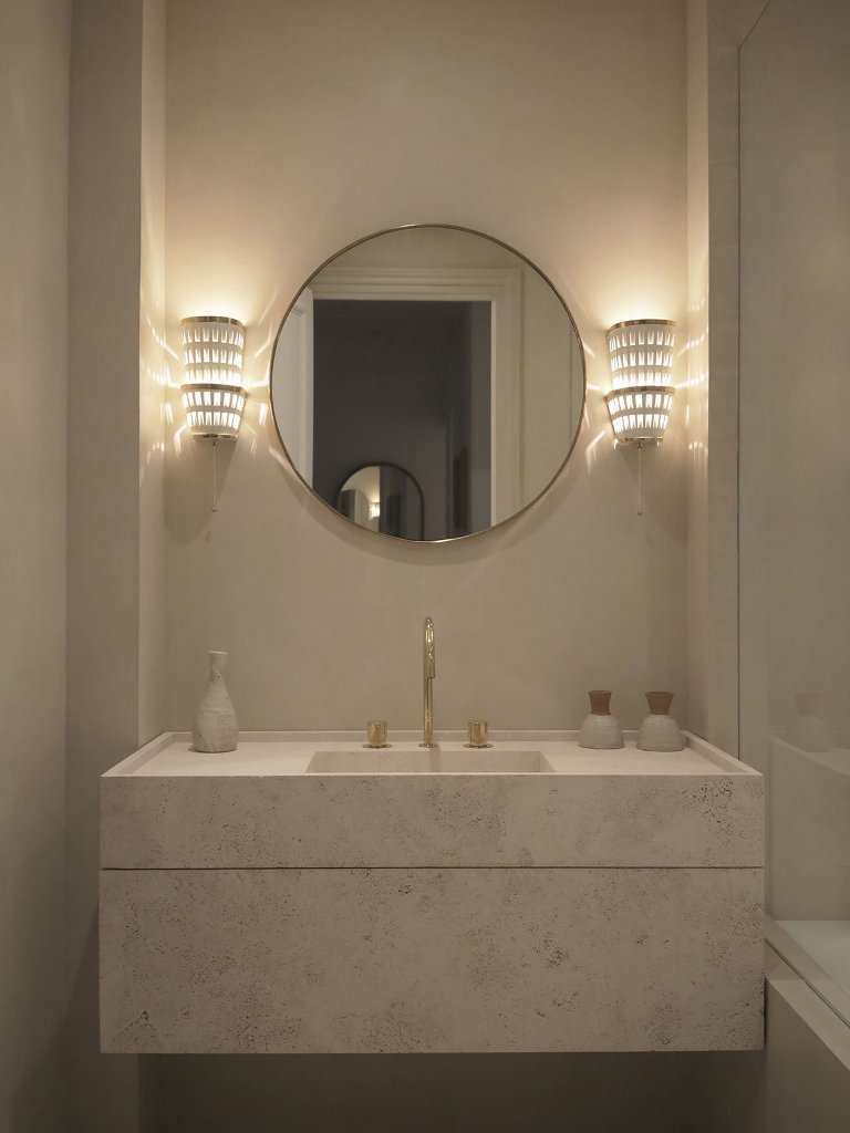 The bathroom is neutral, with a marble vanity, gold fixtures and chic wall sconces