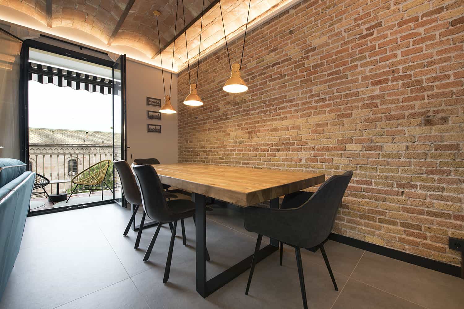 06 The dining space is industrial, with a brick wall, a wooden table and black chairs plus pendant lamps